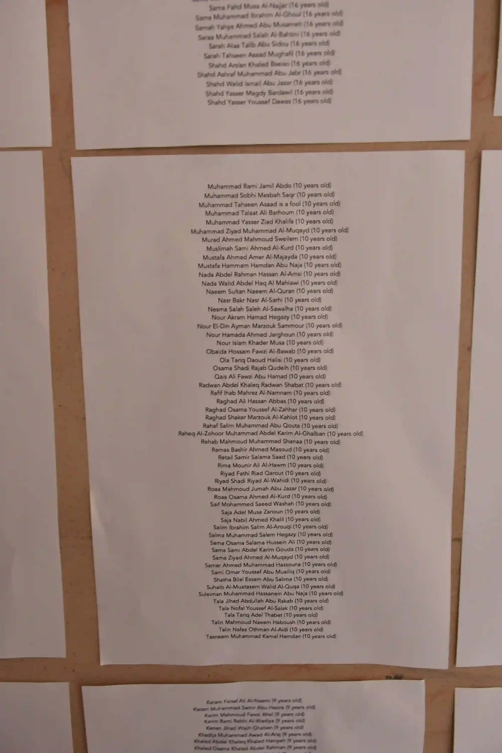 Photographs of individual lives lost showing their ages in the Gaza conflict printed out in lists and placed on stonework of memorial at the University of Edinburgh