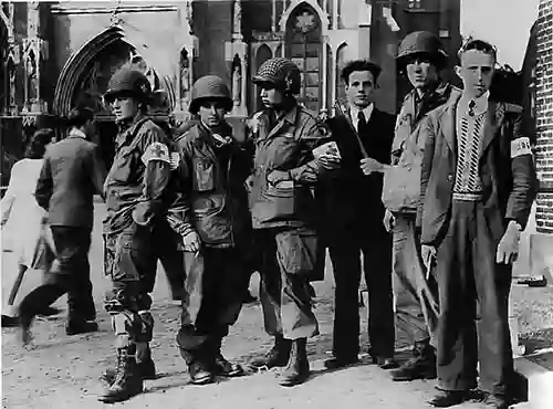 Members of the Veghel Resistance with troops of the United States 101st Airborne Division in Veghel in front of the Lambertus church during Operation Market Garden, September 1944. The Dutch resistance fighters are Bert van Roosmalen and Janus van de Meerakker from the village Eerde.